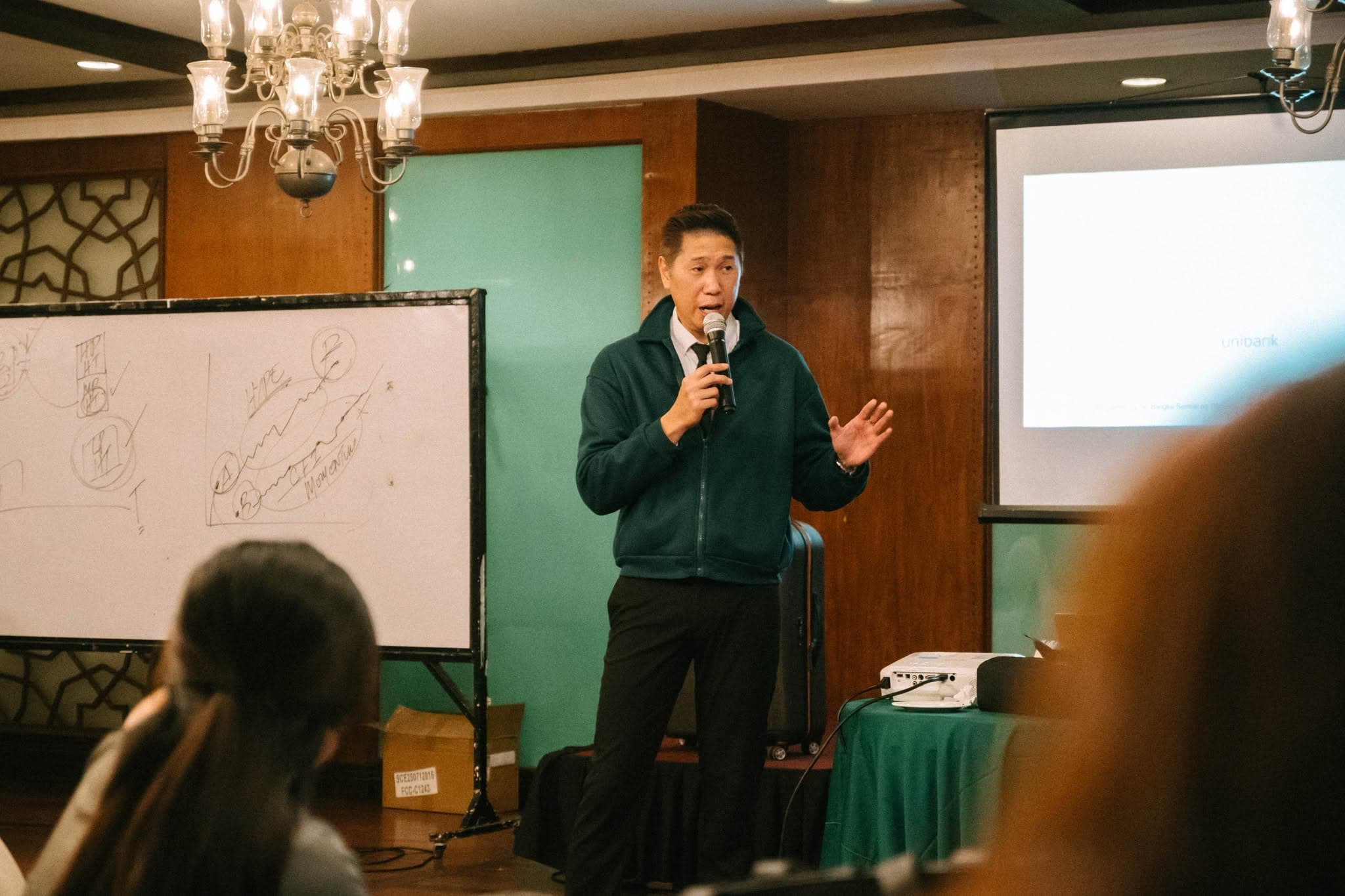 Adrian speaking beside a whiteboard and screen